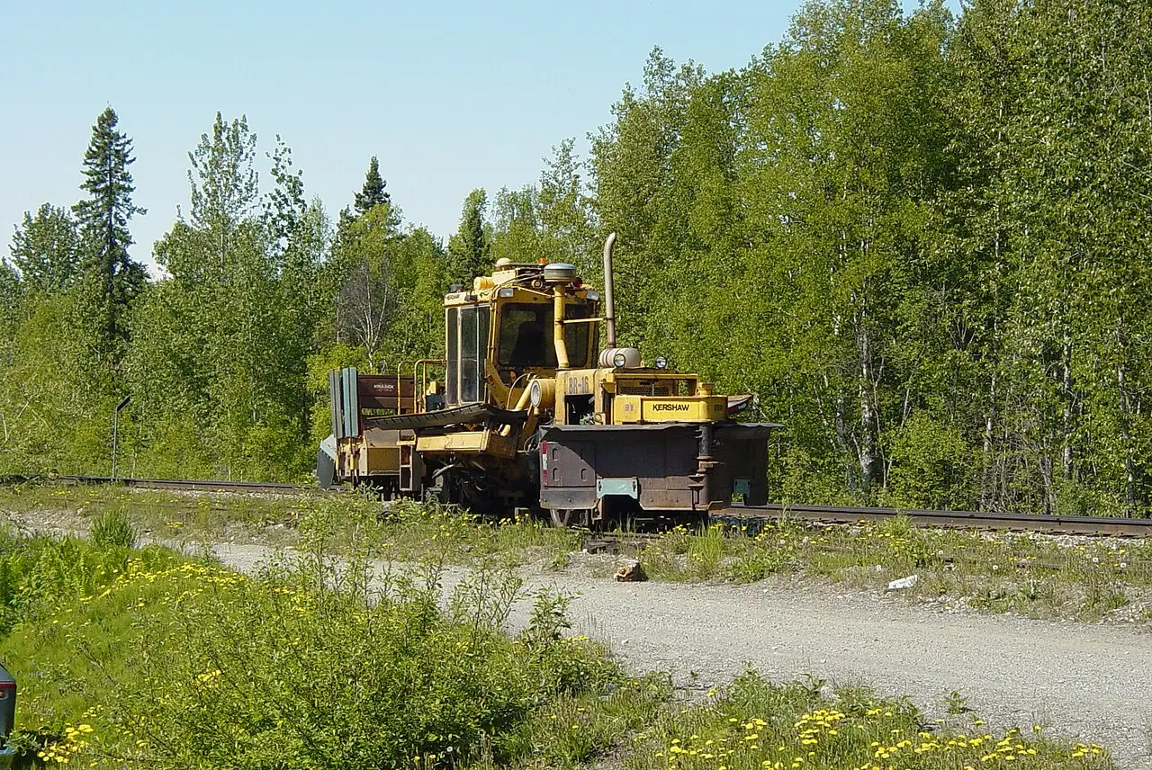 Track machine staged on single track beside a boreal treeline